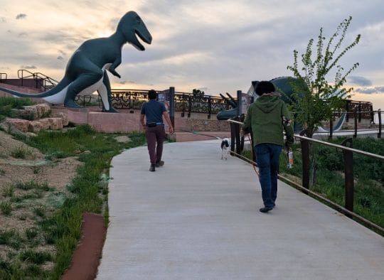 Two men and thier dogs walking up the accessible path at Dinosaur Park