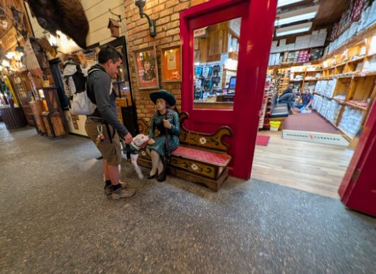 dog investigating a photo op statue inside Wall drug with one more dog looking on (in backpack)