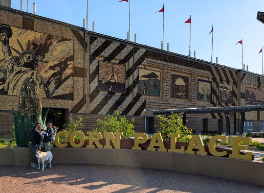 2 people and 3 dogs in front of Corn Palace sign and side of building