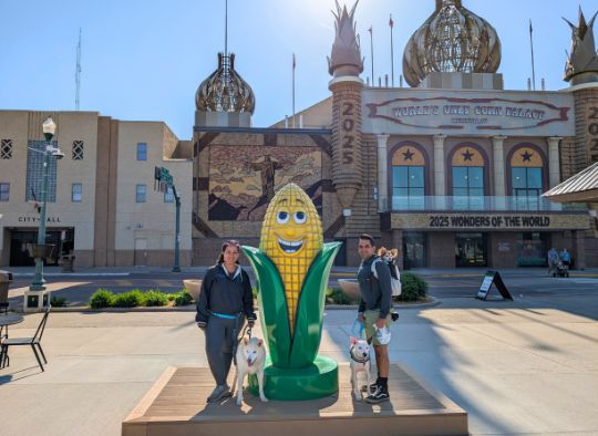 Family (2 human adults and 3 dogs) posing with a corn statue in front of the Corn Palace