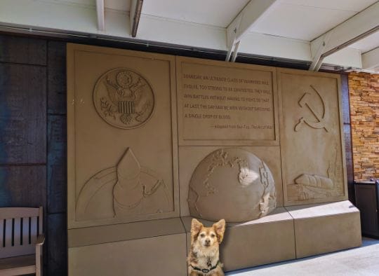 A Small dog in front of outdoor feature of visitor center at Minuteman Missile Silo